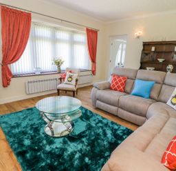 A living room with a glass coffee table and a teal rug by a grey sofa with colorful pillows at Berwyn in Talybont