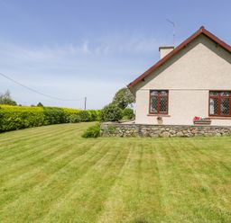 A side view of a house with a lawn and hedges at Berwyn in Talybont