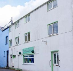 A white building with green trim and a sign reading Ocean Glade next to a blue building at The Old Brewery in Saundersfoot