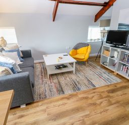 A living room with a grey sofa and yellow armchair next to a white coffee table and shelves with a TV at The Old Brewery in Saundersfoot