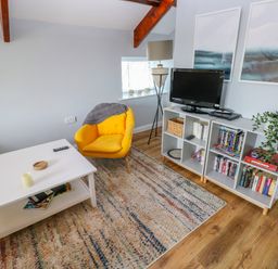 A living room with a yellow chair a white coffee table a television on a white shelving unit and a floor lamp at The Old Brewery in Saundersfoot