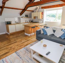 An open plan living room and kitchen with wooden beams a grey sofa and a wooden kitchen island at The Old Brewery in Saundersfoot