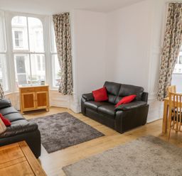 A living room with two black sofas and red pillows wooden furniture and patterned curtains at 1 Church Square in Whitby