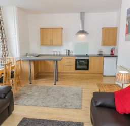A kitchen with wooden cabinets and a dining table next to a living area with dark sofas and red pillows at 1 Church Square in Whitby