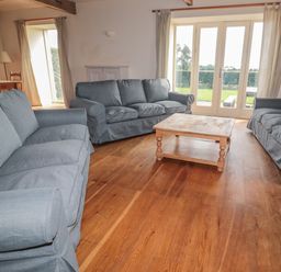 A living room with three blue sofas a wooden coffee table wooden floor and large glass doors at The Long Barn in Berwick-Upon-Tweed