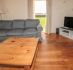 A living room with a grey sofa wooden coffee table TV on a white stand and a floor lamp at The Long Barn in Berwick-Upon-Tweed