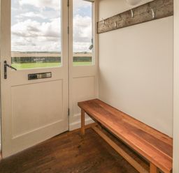An entryway with a wooden bench and wall hooks next to glass doors overlooking a field at The Long Barn in Berwick-Upon-Tweed