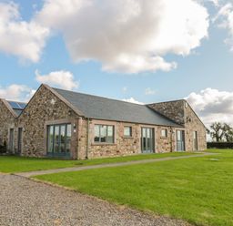 A stone building with multiple windows and doors surrounded by grass and a gravel path at The Long Barn in Berwick-Upon-Tweed