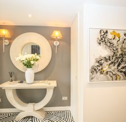 A hallway with a stone console table with a round mirror above two wall lamps and abstract painting on the side wall at Shutts House Garden Apartment in Coombe Bissett