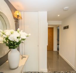 A hallway with a vase of white flowers on a table and a round wall mirror at Shutts House Garden Apartment in Coombe Bissett