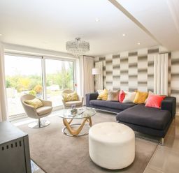 A living room with a black sectional sofa with colorful cushions two grey chairs a round glass coffee table and a white ottoman at Shutts House Garden Apartment in Coombe Bissett