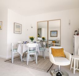 A dining area with a round table set for four and a white swivel chair with a yellow pillow at Sea Point in Exmouth