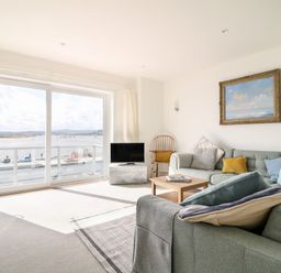 A living room with a gray sectional sofa a wooden chair a small wooden coffee table a flat screen TV and a large sliding glass door overlooking water at Sea Point in Exmouth