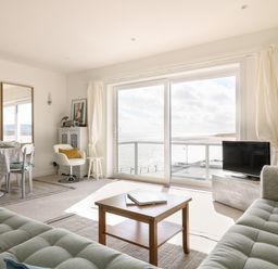 A living room with two gray sofas a wooden coffee table a dining table with chairs and large sliding glass doors overlooking the sea at Sea Point in Exmouth