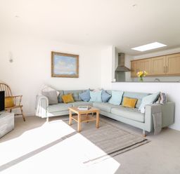 A living room with a sectional sofa pillows a wooden chair a small table a television and a kitchen counter with wooden cabinets at Sea Point in Exmouth