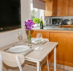 A kitchen with wooden cabinets dining table set with plates glasses and a vase with flowers at Thirley Beck Lodge in Harwood Dale