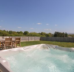 An outdoor space with a hot tub and a wooden table with chairs on a patio at Elan Valley Welsh - The Sheepfold Llanyre near Llandrindod Wells