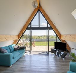 A living room with teal sofas a television and large triangular windows opening to a garden at Elan Valley Welsh - The Sheepfold in Llanyre near Llandrindod Wells