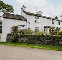 A white stone cottage with multiple windows and a stone wall in front at Rusland View Rusland near Newby Bridge