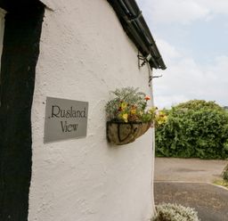 A white wall with a sign reading Rusland View and a hanging basket with flowers and greenery outside Rusland View Rusland near Newby Bridge