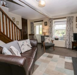 A living room with a leather sofa and armchair beside a wooden staircase and window with curtains at Rusland View Rusland near Newby Bridge