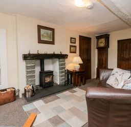 A living room with a fireplace a brown leather sofa and a grandfather clock at Rusland View Rusland near Newby Bridge