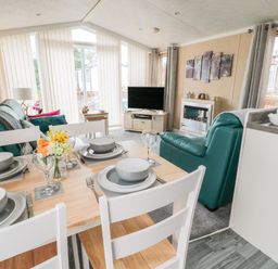 A dining table set with plates and glasses next to a living area with green chairs a TV and a fireplace at Ramblers Rest in Felton