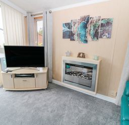 A living room with a television on a cabinet next to a modern fireplace and a teal sofa at Ramblers Rest in Felton