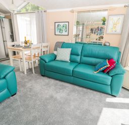 A living room with teal sofas a dining table set and a refrigerator at Ramblers Rest in Felton