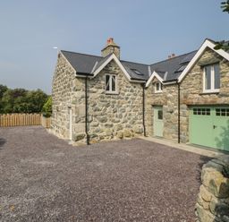 A stone house with a slate roof and green doors and windows with a gravel driveway and wooden fence at Tyn Ffynnon in Dyffryn Ardudwy