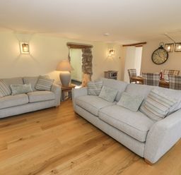 A living room with two gray sofas and pillows beside a wooden dining table with checked chairs at Tyn Ffynnon in Dyffryn Ardudwy