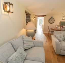 A living room with two sofas with cushions a lamp mounted wall lights wooden floor and a dining table with chairs at Tyn Ffynnon in Dyffryn Ardudwy