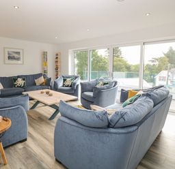 A living room with blue sofas and armchairs around a wooden coffee table next to large sliding glass doors at Argraig in Llanbedrog