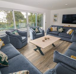 A living room with blue sofas and armchairs around a wooden coffee table and a wall-mounted television at Argraig in Llanbedrog