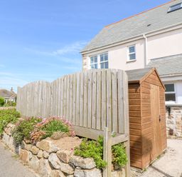 A wooden shed near a stone wall with plants and a wooden fence beside a house at Henrys Croft in Lizard