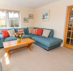 A living room with a blue sectional sofa red and beige cushions a wooden coffee table with flowers and paintings on the wall at Henrys Croft in Lizard