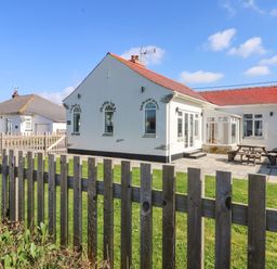 A white single-story house with a red roof and patio area behind a wooden fence at Senafe in Widemouth Bay