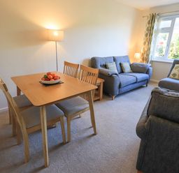 A living room with a wooden dining table and chairs a bowl of fruit two sofas an armchair a floor lamp and a window at Fairfell in Keswick