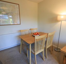 A dining area with a wooden table and four chairs a bowl of fruit on the table a floor lamp and a framed map on the wall at Fairfell in Keswick