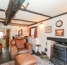 A living room with a leather armchair and ottoman near a fireplace with a wood stove at Combe Cottage in Brimscombe near Stroud