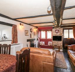 A living room with brown leather sofas a wooden dining table a fireplace and a wall-mounted television at Combe Cottage in Brimscombe near Stroud
