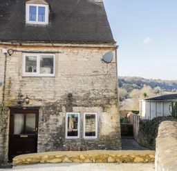 Stone exterior of a house with windows and a door and a satellite dish at Combe Cottage in Brimscombe near Stroud