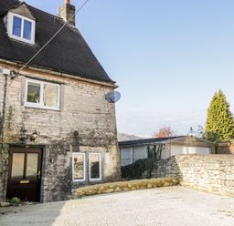 The exterior of a stone house with a wooden door driveway and a stone wall at Combe Cottage in Brimscombe near Stroud
