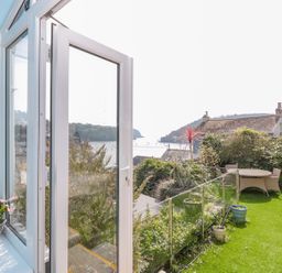 A garden area with a round table and chairs overlooking water and hills at Estuary View House and Annexe in Dartmouth