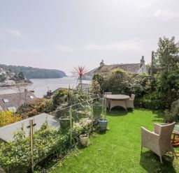 A garden with outdoor seating and potted plants overlooking a river and houses at Estuary View House and Annexe in Dartmouth