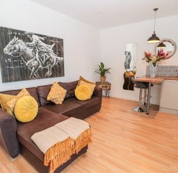 A living room with a brown sofa and yellow cushions a small dining area with two stools and a vase of flowers at The Snug in Beadnell