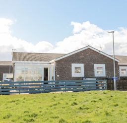 A single-story brick house with a blue fence and a grassy lawn in front at The Snug in Beadnell