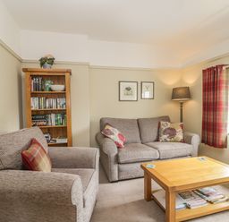 A living room with a sofa and armchair a wooden coffee table bookshelf and window with curtains at Stakesby House Apartment 3 Whitby