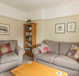 A living room with an armchair, a sofa with cushions, a wooden bookshelf, a coffee table, and framed pictures on the wall at Stakesby House Apartment 3 Whitby