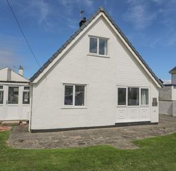A front view of a white detached house with windows a door and a driveway with grass at Crows Nest - Rhosneigr in Rhosneigr